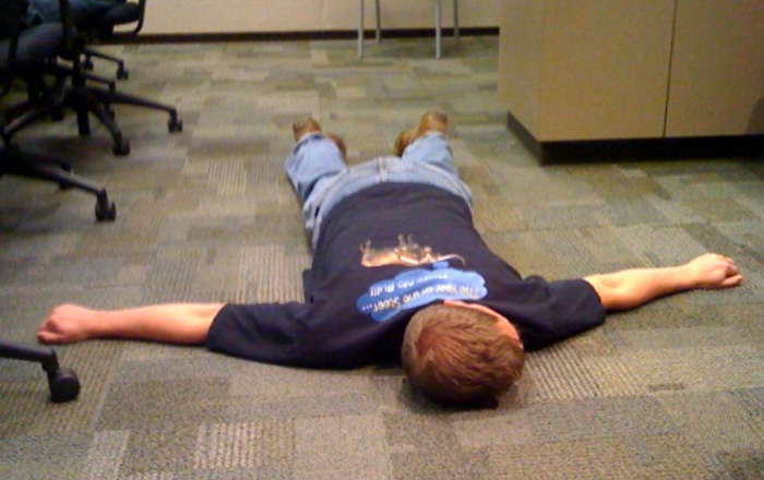 Young man lying flat on his face on a carpeted floor.